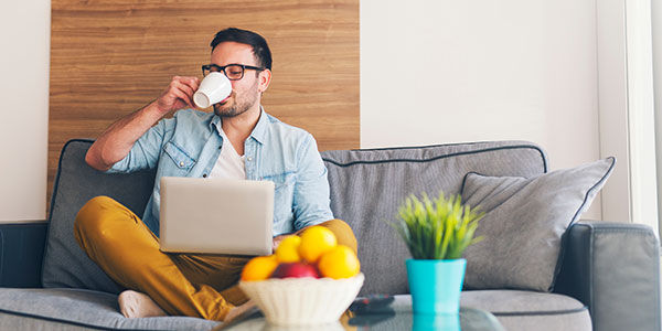 Man working from home on his sofa with a laptop and cup of coffee.